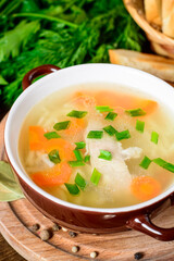 Homemade chicken soup with noodles and vegetables in ceramic bowl on wooden table.