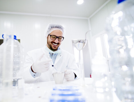 Smiling laboratory technician doing chemical analysis. Wearing sterile uniform .