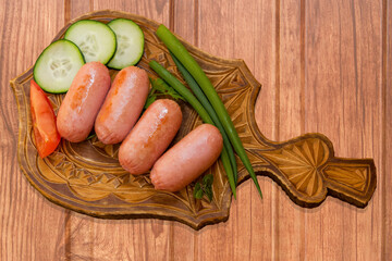 Breakfast of fried mini sausages with vegetables on the background of beige wooden table vintage top view