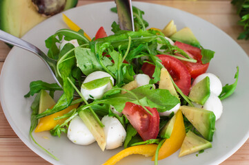 Fresh salad with cherry tomatoes, rucola, mozzarella and bulgarian pepper. Wooden background. Top view. Close-up