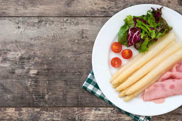 White asparagus with salad and ham on wooden background
