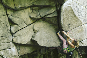 Young attractive female rock climber climbing challenging route on steep rock wall against scenic sunset background.