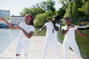 Three stylish african american friends, wear on white clothes at pier on beach showing dab. Street fashion of young black people. Black man with two african girls.