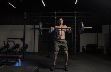 Fototapeta na wymiar Muscular White Caucasian man doing barbells snatch exercise in a dark grungy gym wearing shorts and showing muscular body and six pack abs 