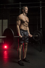 Fototapeta na wymiar Muscular White Caucasian man doing a barbell bicep curl in a dark grungy gym wearing shorts and showing muscular body and six pack abs 