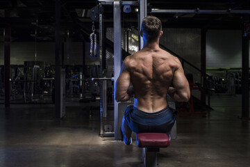 Fototapeta na wymiar Muscular White Caucasian man performing a back rowing exercise in a dark grungy gym wearing shorts and showing muscular back