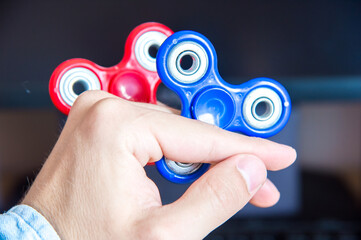 Man's hand holds two multi-colored spinners on the background of a personal computer close-up