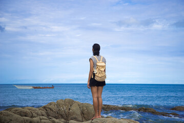 Fototapeta na wymiar Lonely girl stand on the rock beach and looking to the tropical sea