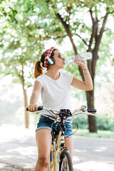 Naklejka premium Young woman drinking water sitting on the bicycle