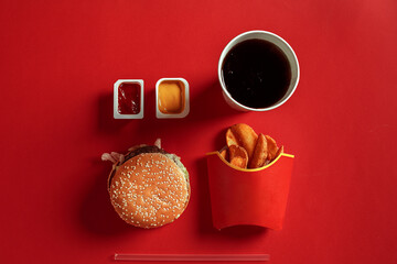 Concept of mock up burger, potatoes, sauce and drink on red background. Copy space for text and logo.