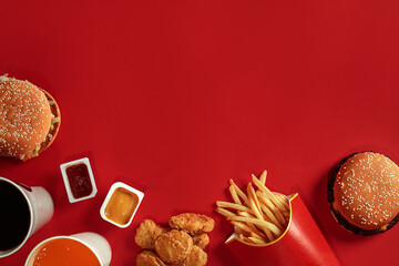 Two hamburgers and french fries, sauces and drinks on red background. Fast food. Top view, flat lay with copyspace