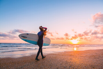 Sporty surf girl go to surfing. Woman with surfboard and sunset or sunrise on ocean