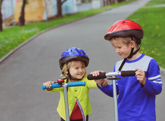 little boy and girl with helmets riding scooters