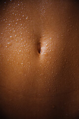 Female navel with drops of water or sweat close up. Wet stomach and navel, human body, sexy belly of young woman. Nude body after shower, moisturizing for skin, skin care, body oil, cosmetics