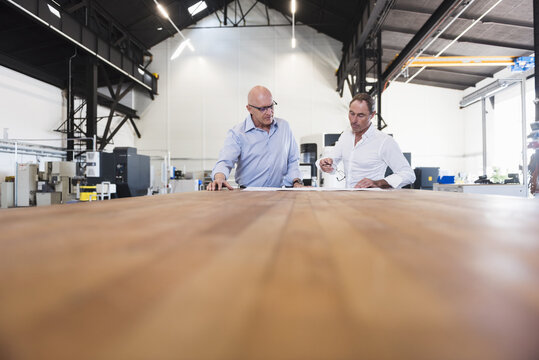 Two businessmen looking at plan on table in factory