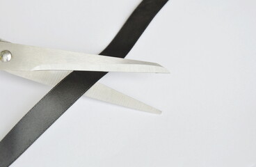 scissors blade cutting black fabric ribbon on white background