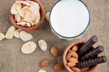 A glass of milk with almond nuts, corn flakes, chocolates,  on sacking background Copy space. Space for text.