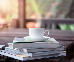 White ceramic coffee cup over the books on a wooden table in the garden with evening sunlight, -Lens flare filter.