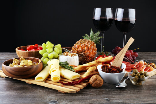 Tapas or Italian antipasti wine snacks set. Cheese variety, Mediterranean olives, pickles, Prosciutto di Parma with grapes, wine in glasses over black grunge background