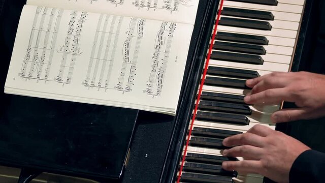 Pianist Playing / Piano Player / Orchestra Musician. Pianist plays piano at a classical music concert. Music sheets of VII century classics (now public-domain). Hands and keyboard close-up.