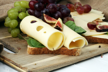 Bread with slices of cheese, some grapes and fig for lunch table. Sharing antipasti on party or summer picnic time