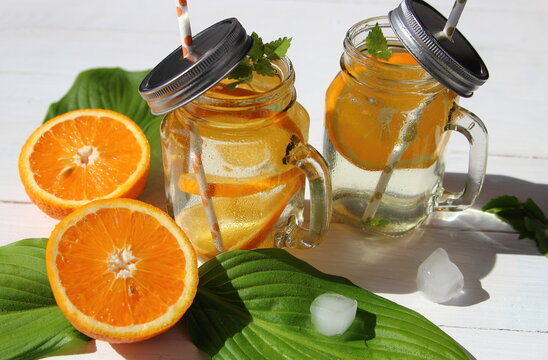 Апельсиновый лимонад с каплями воды  на зеленом листе и белом деревянном фоне. 