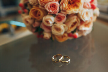 Obraz na płótnie Canvas Wedding gold rings on a transparent table and a wedding bouquet