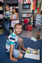 Portrait of happy schoolboy reading book in library