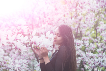 Adorable girl with brunette, long hair enjoying magnolia flower blossom