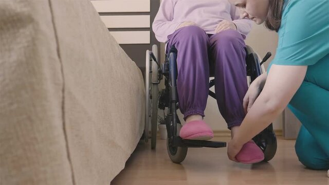 Young nurse caring of elder disabled woman in wheelchair and going for a walk. Home or hospice nursing and assistance concept. 4K footage at 60fps.