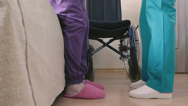 Young nurse caring of elder disabled woman in wheelchair. Home or hospice nursing and assistance concept. 4K footage at 60fps.
