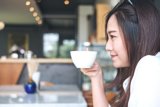 Closeup image of a beautiful Asian woman smelling and drinking hot coffee with feeling good in modern cafe