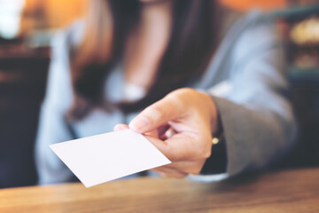 A beautiful Asian business woman holding and giving empty business card in modern loft cafe