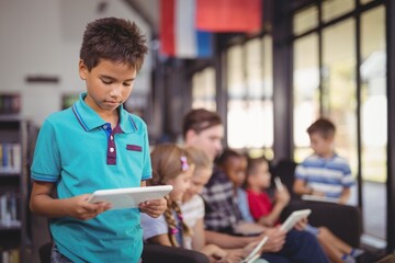 Attentive schoolboy using digital tablet in library