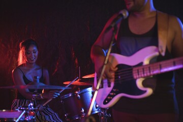 Obraz na płótnie Canvas Male playing guitar with female drummer in nightclub