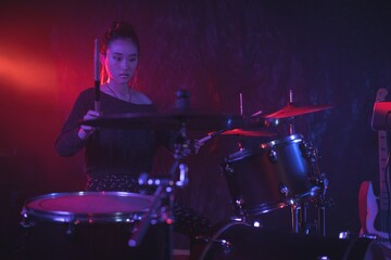 Fototapeta na wymiar Female drummer playing drum kit in illuminated nightclub
