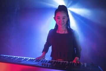 Female musician playing piano in illuminated nightclub