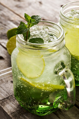 Tasty cold fresh drink lemonade with lemon, mint, ice and lime in glass on wooden table. Closeup.