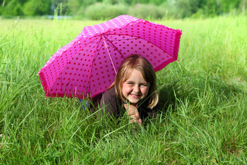 Uśmiechnięta dziewczynka leży na trawie z parasolką.