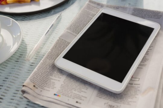 Digital tablet with newspaper on table at cafe