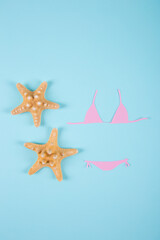 Fototapeta na wymiar Pink paper bikini swimsuit with two starfishes on blue background. Minimalistic summer flat lay.