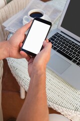 Cropped hands of person holding mobile phone by laptop at cafe