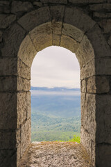 Arch window in the old stone fortress, mountains and sky view