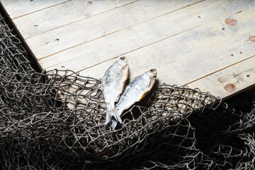 Sun dried fish and fishing nets on the wooden background.