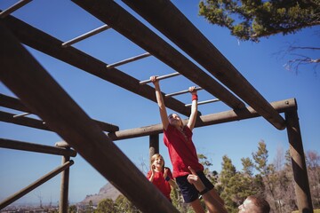 Fototapeta na wymiar Trainer assisting girl to climb horizontal bars 