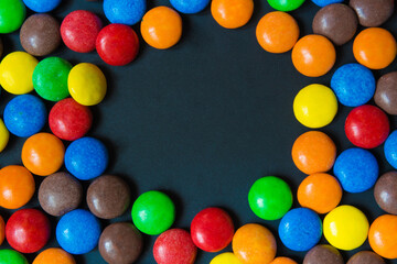 Multicolored sweets in the form of a dragee on a dark background pattern frame background