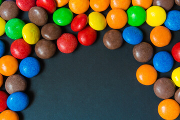 Multicolored sweets in the form of a dragee on a dark background pattern frame background