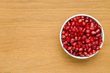 Grains Of Pomegranate In A White Bowl On A Wooden Board. Close-Up. Free Space For Text. Top View. Right Version.