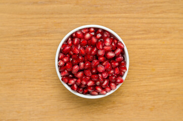 Grains Of Pomegranate In A White Bowl On A Wooden Board. Close-Up. Free Space For Text. Top View. In The Center.