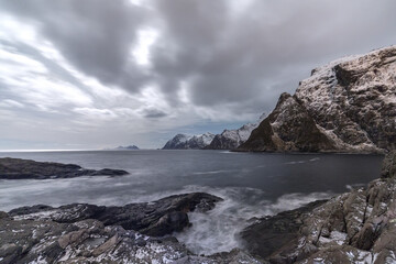 Obraz premium Cloudy sky above the mountains partially snowy and the cold sea. Lofoten Islands. Northern Norway. Europe
